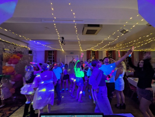 A busy dance floor at a UV party with people holding glow sticks under neon lights.